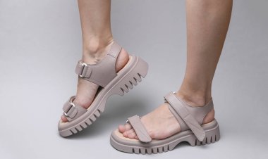 Female legs in leather sandals on a gray background
