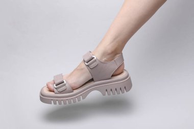 Female leg in leather sandal on a gray background