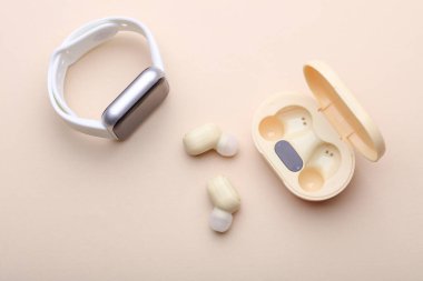 Wireless Earphones with Charging Case, smart watch on Beige Background. Modern gadgets