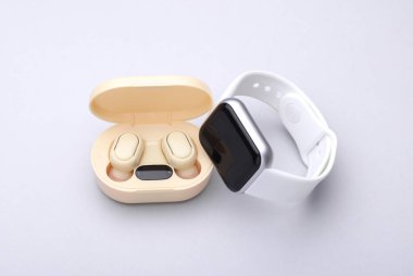 Wireless Earphones with Charging Case, smart watch on gray background. Modern gadgets