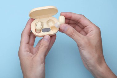 Hands holding Wireless Earphones with Charging Case on blue Background