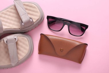 Yaz güneşlikleri ve pembe arka planda güneş gözlüklü deri çanta. Düz yatıyordu