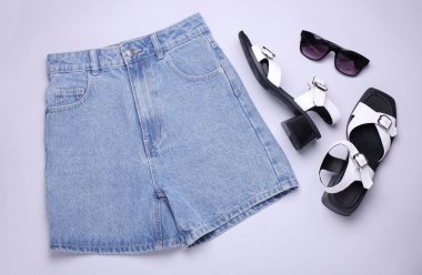 Kadın yaz aksesuarları ve giysileri. Kum şortu, sandalet ve gri arka planda güneş gözlüğü. Üst görünüm