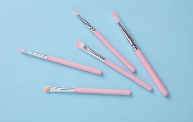 Set of pink makeup brushes on a blue background