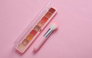 Makeup brush with eye shadow palette on pink background