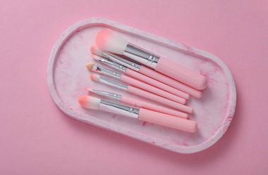 Set of makeup brushes in tray on pink background