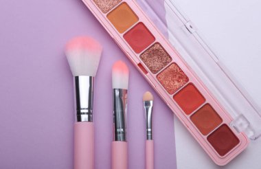Makeup brushes with eye shadow palette on purple white background