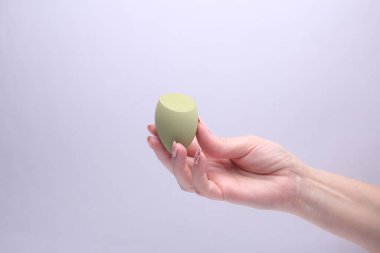 Gri arka planda makyaj süngeri tutan kadın.