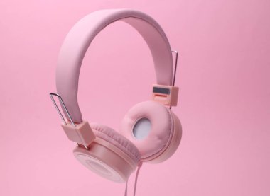 Pembe arka planda izole edilmiş yüzen stereo kulaklıklar.