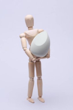 Gri arka planda makyaj süngeri tutan tahta kukla.