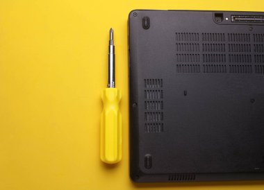 Bilgisayar tamiri. Sarı arka planda tornavidalı dizüstü bilgisayar