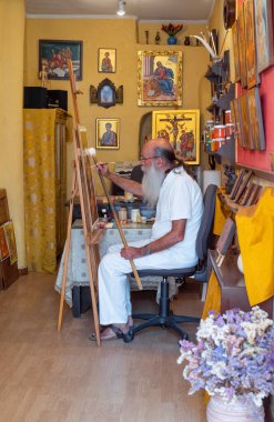 Mykonos, Yunanistan - 6 Temmuz 2017: Chora eski köyünün bir ara sokağına geleneksel ikonlar çizen yaşlı bir sanatçı