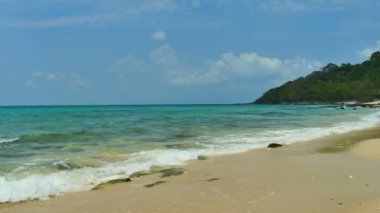 Deniz dalgaları, kumlu sahil ve mavi gökyüzü olan pitoresk bir marina.