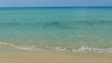 Deniz dalgaları, kumlu sahil ve mavi gökyüzü olan pitoresk bir marina.