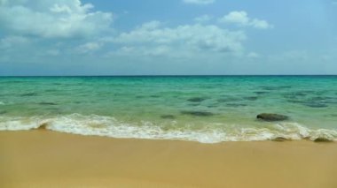 Deniz dalgaları, kumlu sahil ve mavi gökyüzü olan pitoresk bir marina.