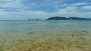 Deniz dalgaları, kumlu sahil ve mavi gökyüzü olan pitoresk bir marina.