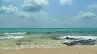 Deniz dalgaları, kumlu sahil ve mavi gökyüzü olan pitoresk bir marina.