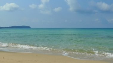 Deniz dalgaları, kumlu sahil ve mavi gökyüzü olan pitoresk bir marina.