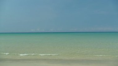 Deniz dalgaları, kumlu sahil ve mavi gökyüzü olan pitoresk bir marina.