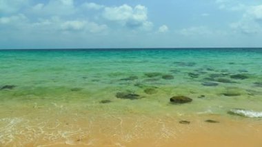 Deniz dalgaları, kumlu sahil ve mavi gökyüzü olan pitoresk bir marina.