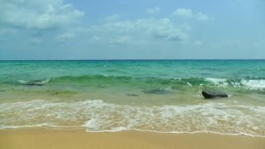 Deniz dalgaları, kumlu sahil ve mavi gökyüzü olan pitoresk bir marina.