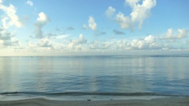 Deniz dalgaları, kumlu sahil ve mavi gökyüzü olan pitoresk bir marina.