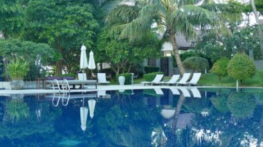 Yüzme Havuzu, plaj şemsiyeleri ve yemyeşil tropik bitki örtüsü 