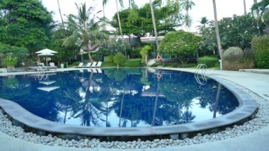 Yüzme Havuzu, plaj şemsiyeleri ve yemyeşil tropik bitki örtüsü 