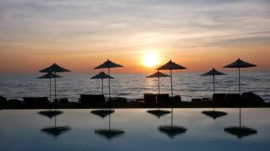 Güneş şemsiyeleri ve deniz ve havuz üzerinde gün batımı manzarası