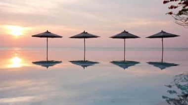 Güneş şemsiyeleri ve deniz ve havuz üzerinde gün batımı manzarası
