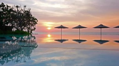 Güneş şemsiyeleri ve deniz ve havuz üzerinde gün batımı manzarası