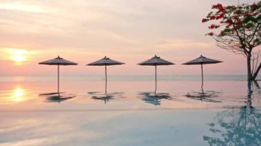 Güneş şemsiyeleri ve deniz ve havuz üzerinde gün batımı manzarası