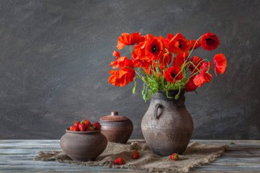 Natürmort. Bir demet chamomiles, çilek ve tahta bir masanın üzerinde kil sürahi.