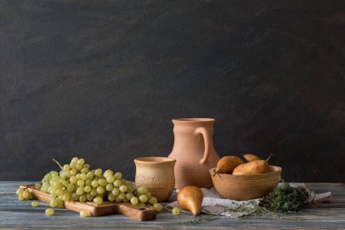 Köy tarzında sakin bir hayat: ahşap bir masada bir dizi kil tabak, üzüm ve armut. Pencerelerden gelen doğal ışık.