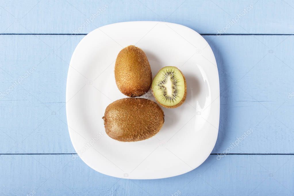 Kiwi fruits on white plate and on wooden blue table. Top view. Copy space.
