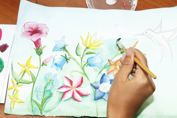 Girl draws flowers with watercolor paint on paper.