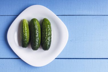 Taze yeşil salatalık beyaz tabakta. Üstten görünüm ahşap tablo. Kopya alanı.