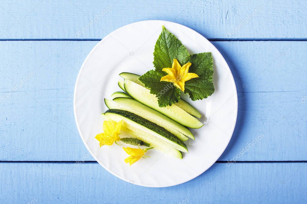 Freshly sliced cucumbers, green leaves and yellow flowers for dietary breakfast or lunch. Vegetarian food concept. Top view.