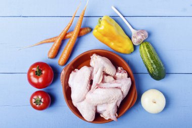 Seramik ürünler ve ahşap masa üzerinde taze organik sebze tavuk kanatları. Üstten görünüm.