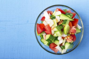 Doğranmış sebze - salatalık, domates ve soğan ahşap masa üzerinde cam kapta. Yukarıdan görüntüleyin. Kopya alanı.