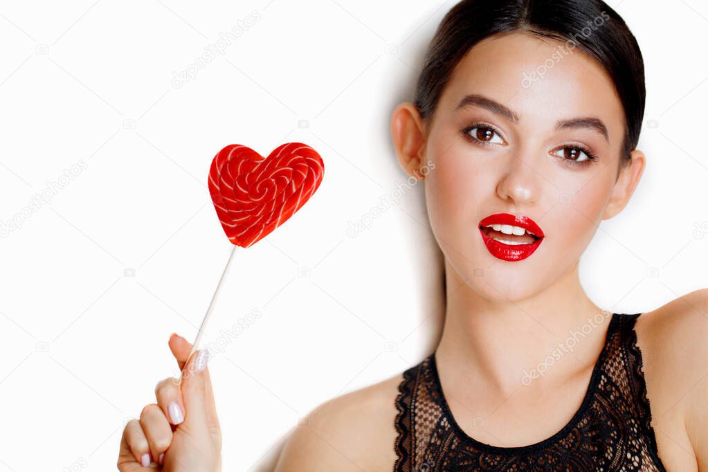 Photo of cheerful woman wearing dress laughing and eating lollipop isolated over white background