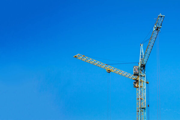 Two cranes against the blue sky. Blue and yellow crane at the construction site.
