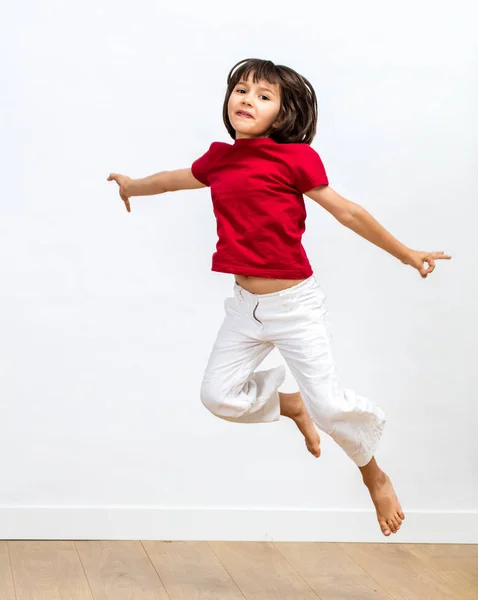 smiling beautiful 6-year old girl jumping and flying high to express freedom, happiness, joy, fun sports and positive energy over wooden floor, white background
