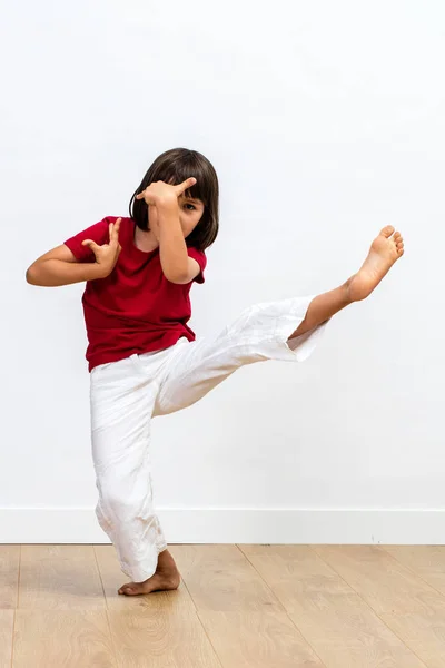 concentrated young child showing grace and positive energy with fighting legs and arms for kid\'s martial art and positive energy over wooden floor, white background