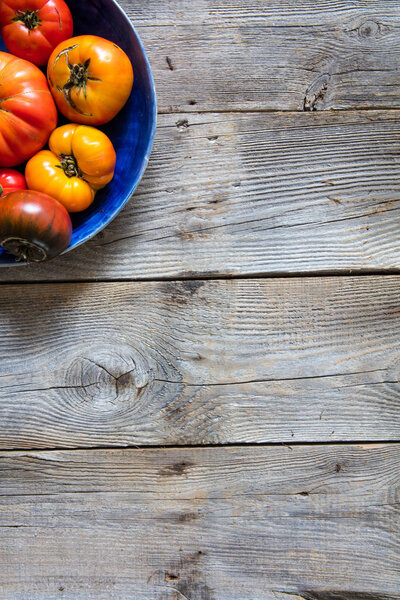 Земляная половинчатая тарелка из цветных потрескавшихся помидоров для органического вегетарианского меню на устойчивом старом деревянном фоне для вертикального вида сверху копировальный баннер пространства
