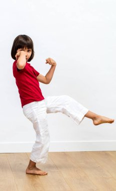 heyecanlı genç çocuk yumruklarını ile onun gücünü gösteren, savaş sanatı, egzersiz zevk yükseltilmiş tai chi, kung fu veya taekwondo eğlenmek için çocuk spor ve enerji ahşap zemin, beyaz arka plan üzerinde