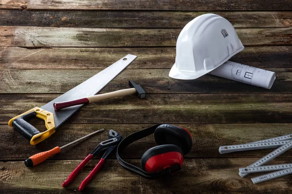House tooling gear for building, maintenance, craftsmanship and repairing with hard hat, architect blue print, safety ear protection and many tools over wood background