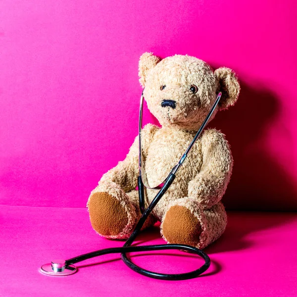 Urso de pelúcia criança com um estetoscópio para cuidados de saúde, fundo rosa — Fotografia de Stock