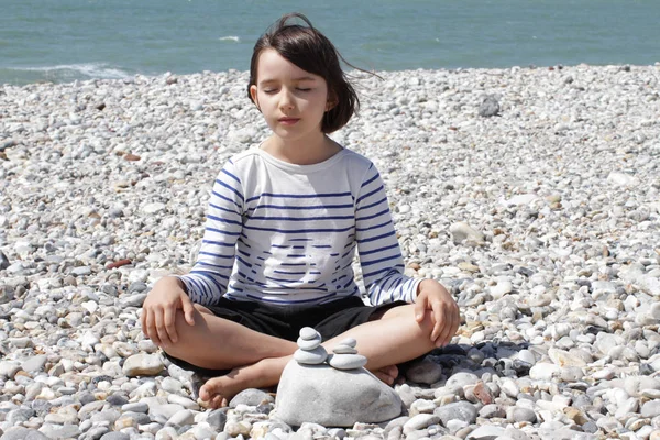 Peaceful child sitting with pebbles for mindfulness and ocean energy — Stock Photo, Image