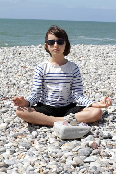 Child with sunglasses meditating with quartz crystals on pebble beach — Stock Photo, Image